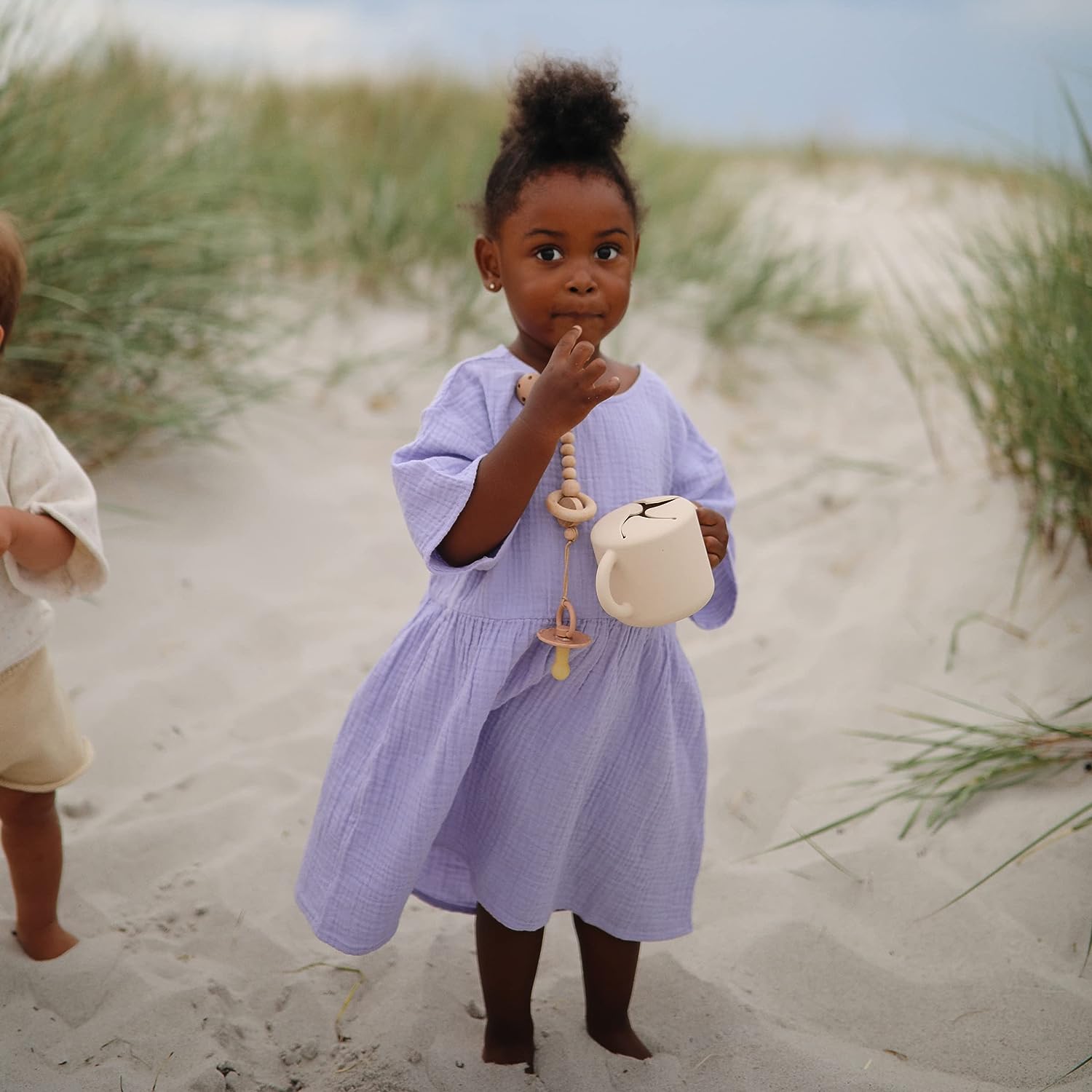 Little girl holds Mushie Silicone Snack Cup - Shifting Sand